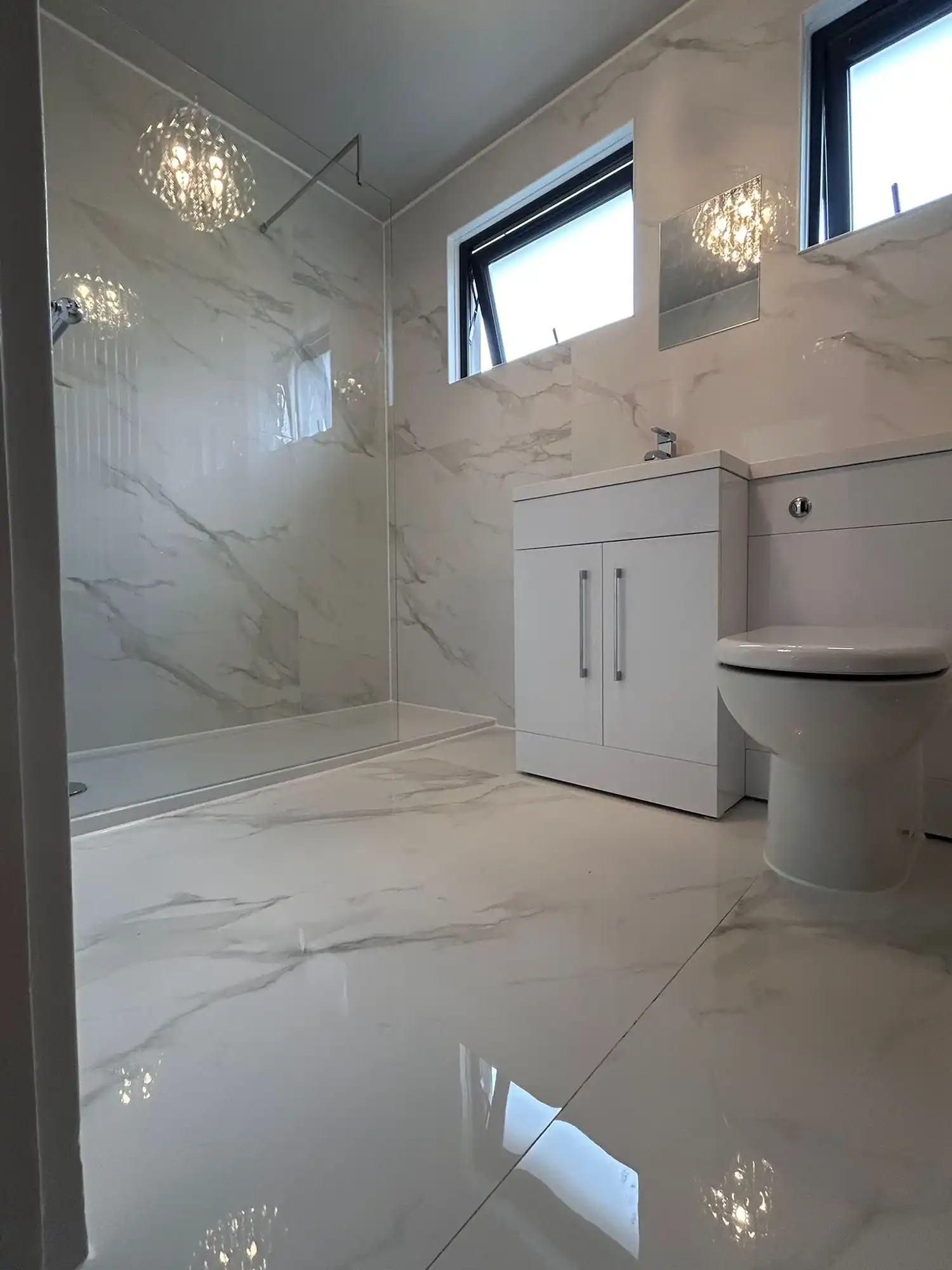 Modern bathroom featuring a shower area, white cabinetry, and marble-patterned tiles with natural light through windows.